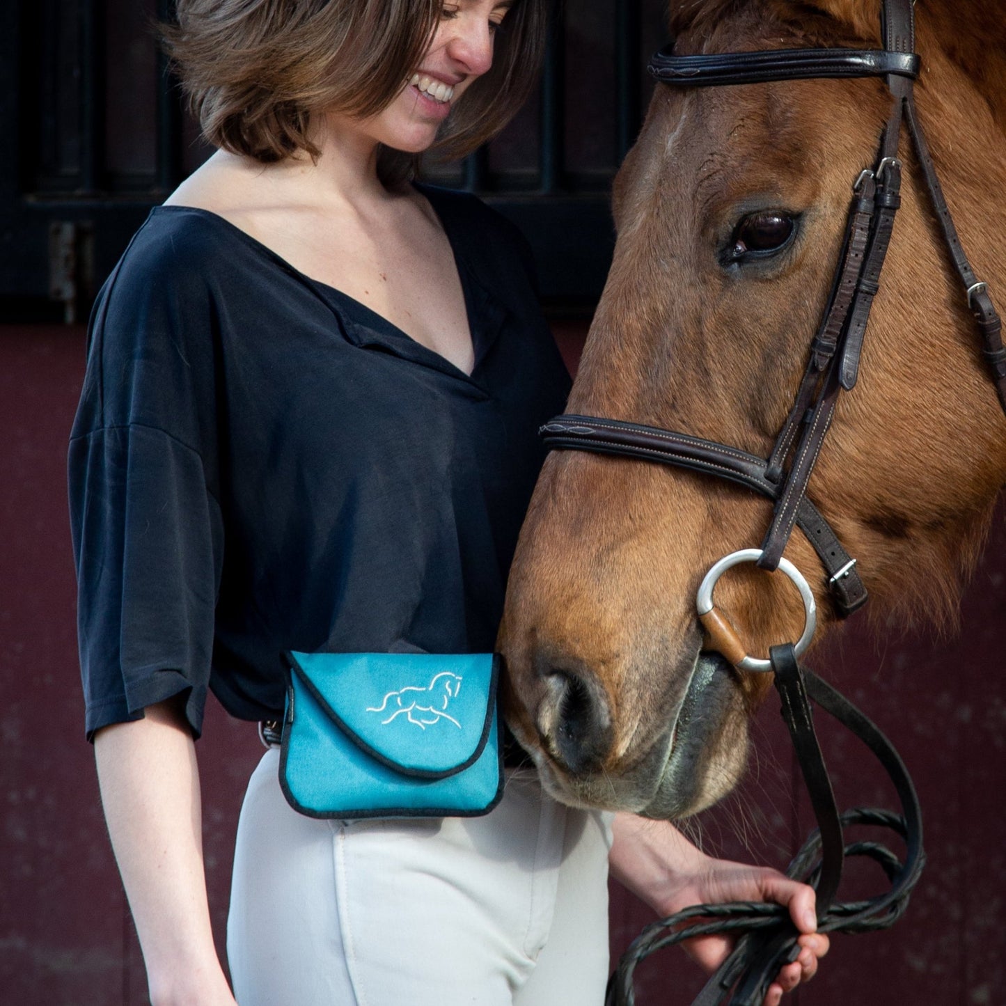 Woman wearing a teal horse treat training bag with brown horse