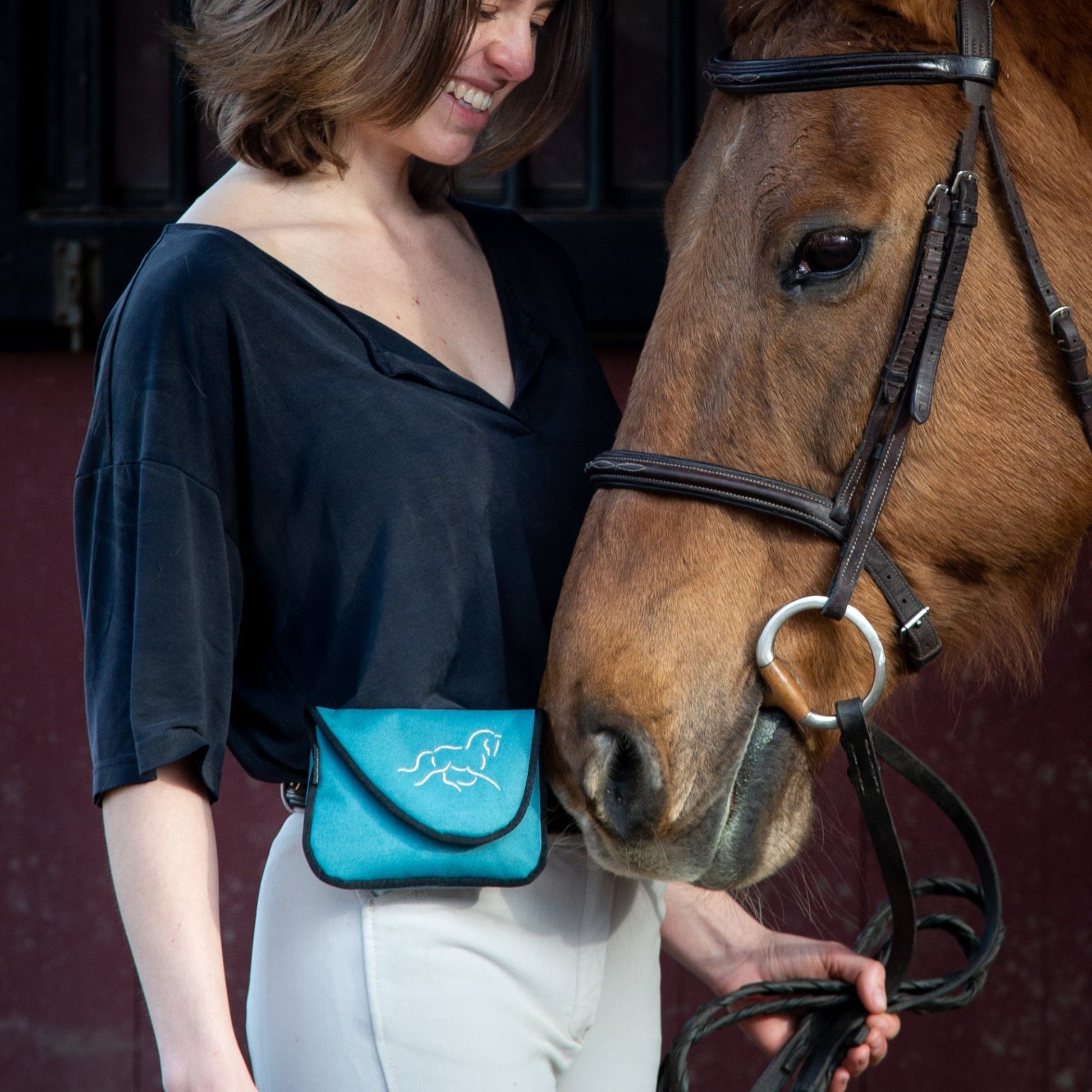 Woman wearing a teal horse treat training bag with brown horse